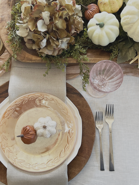 Table setting using chargers, white plates, and antique champagne colored plates with linen napkins and tinted drinking glasses