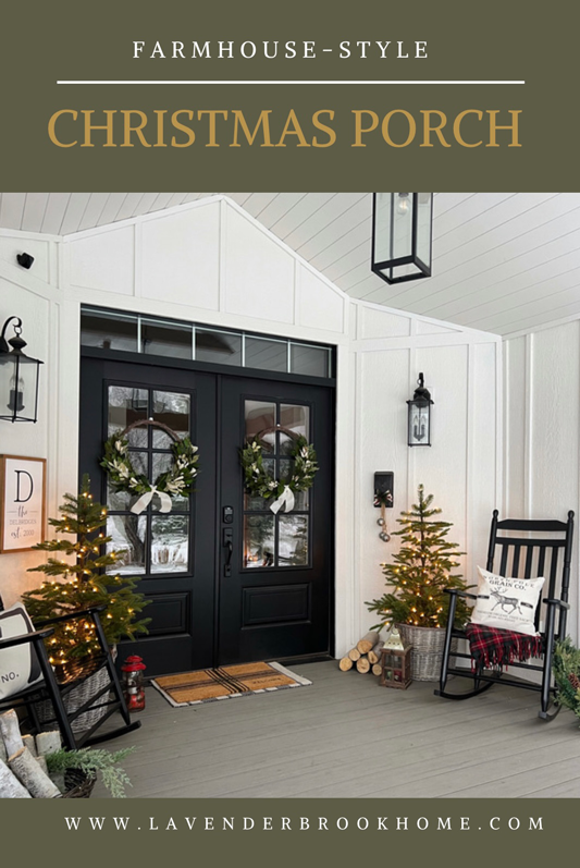 White farmhouse porch with board and batten, shiplap ceiling, wood beams and black lanterns decorated for Christmas. Double black doors decorated with wreaths. Two small Christmas trees on the sides in baskets and with lights. Two black rocking chairs with red and green blankets and pillows. An old wooden sled propped against the wall and a stack of wood beside the sled. 