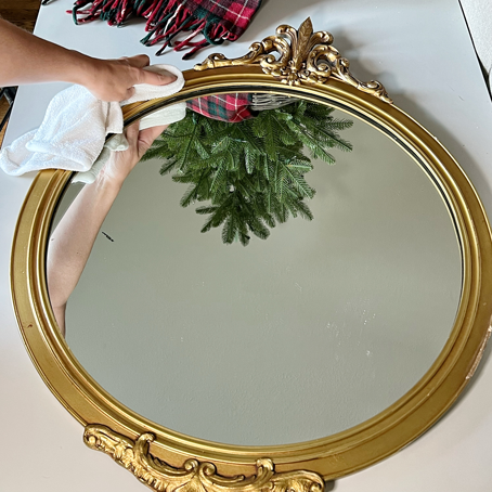 round antique gold mirror with ornate scroll details hand wiping mirror with rag: Rub'-N-Buff Mirror Makeover