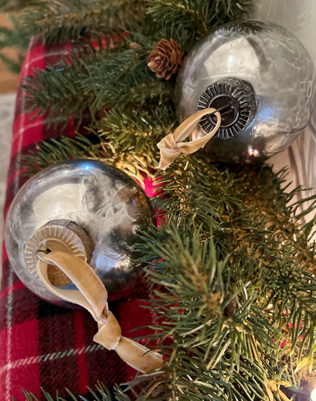 Christmas ornament in twinkling lights on a red plaid blanket. Plastic ornaments that looks like vintage mercury glass in silver and gold.