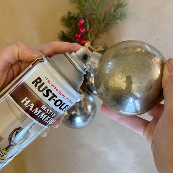 spraying matte black hammered spray paint into a round plastic Christmas ornament bulb