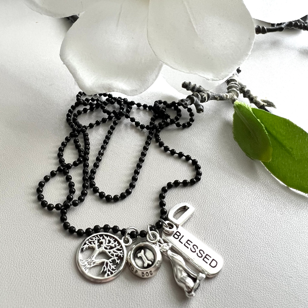 Warmhearted DIY Story Necklaces: Bead ball chain necklace in white bowl with charms. Charms include: tree of life charm, dog bowl charm, blessed pendant, cat charm and the letter D charm.