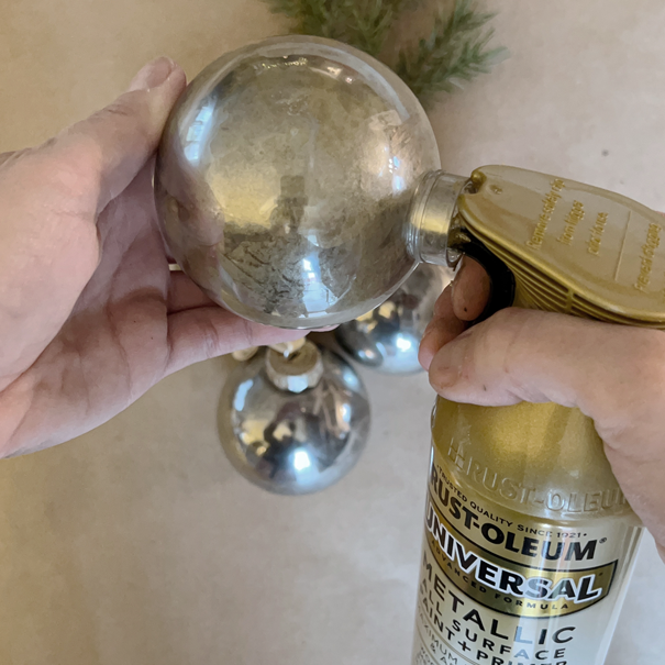 spraying Rust-Oleum gold spray paint into a round plastic Christmas ornament bulb