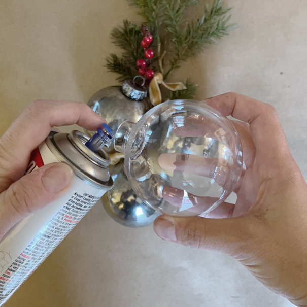spraying Krylon Looking Glass spray paint into a round plastic Christmas ornament bulb