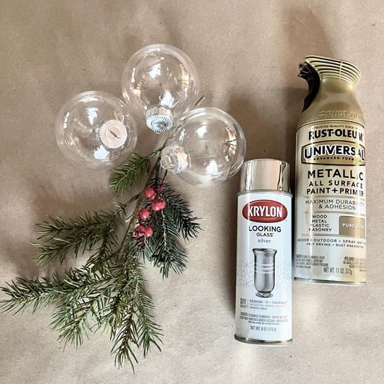 Shatterproof glass-like plastic round Christmas ornaments bulbs with silver caps next to a sprig of greenery and berries, gold spray paint, mirror spray paint