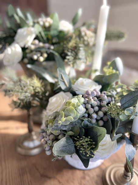 Farmhouse table setting with two winter flower bouquets made of green eucalyptus, green pine, white roses, and green-blue frosted berries.
