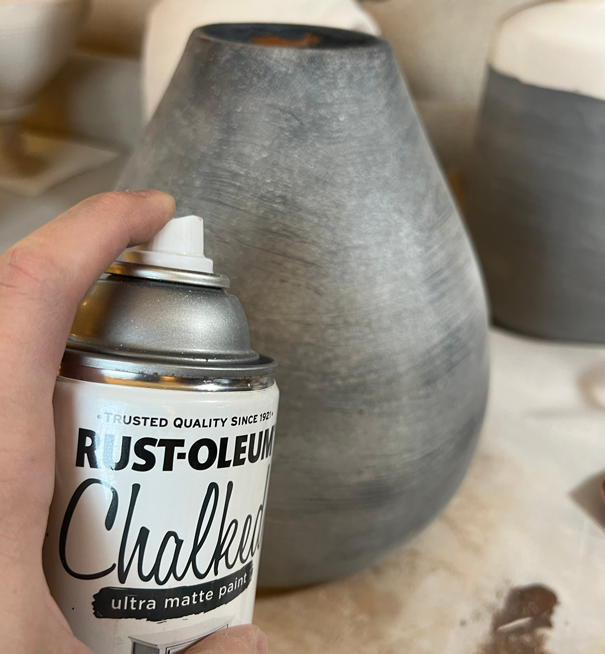 Black chalky pottery with spray paint can in front.