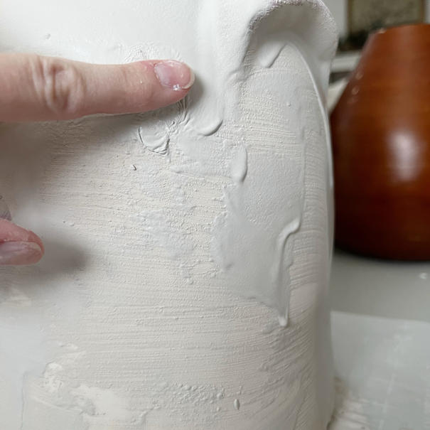 White pottery painted with baking soda and paint mixture. A finger dabs in splotch marks.