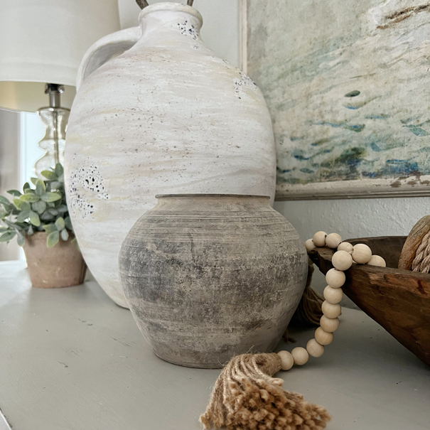 Large white vintage jug with aged wear next to a small black earthen vase with a chalky finish.