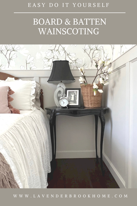 Bedroom with greige board and batten wainscoting and floral wallpaper. A black night stand sits along side the bed with a grey and black lamp, alarm clock and magnolia flowers in a basket. The bed has a ruffled white bedspread.