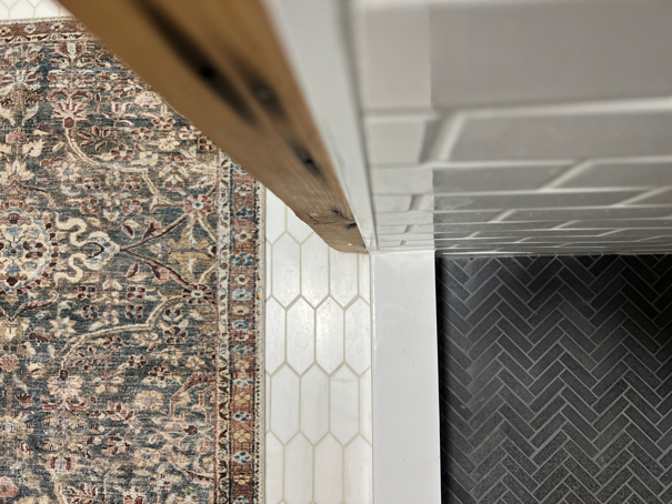 Close up of black matte herringbone shower tile and subway shower wall tile. Hexagon bathroom floor tiles and a vintage Persian rug in multiple colors.