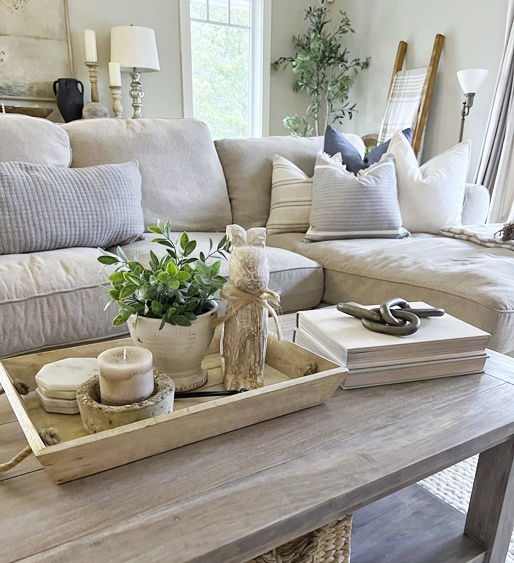 Easy spring decorating ideas a coffee table with a tray filled with a plant, wooden bunny, marble coasters. This in front of a couch with blue and grey throw pillows.