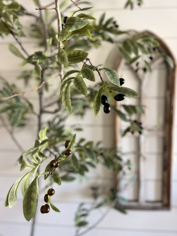 Close up view of a DIY realistic olive tree with arched window in the background.