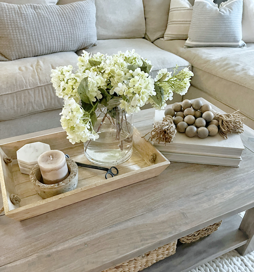 Easy spring decorating ideas overview of hydrangeas in a glass vase with water and siting in a tray. White marble coasters and a concrete candle holder and wick scissors sit beside. 