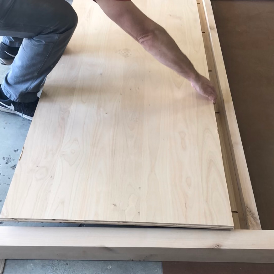 Man laying unfinished plywood panel in wood headboard frame