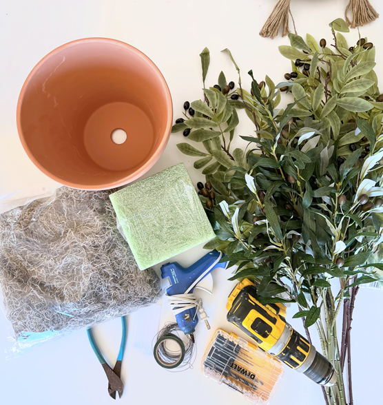 Supplies for a realistic DIY faux tree using a terracotta pot, faux olive branches, wire cutters, hot glue, floral wire, drill and small drill bit, floral foam, and Spanish. moss