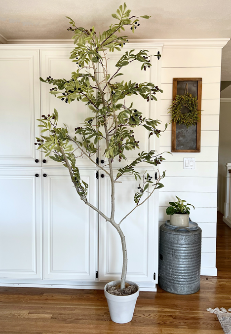 Realistic DIY faux tree finished and sitting floor to ceiling in front of white cabinetry. 