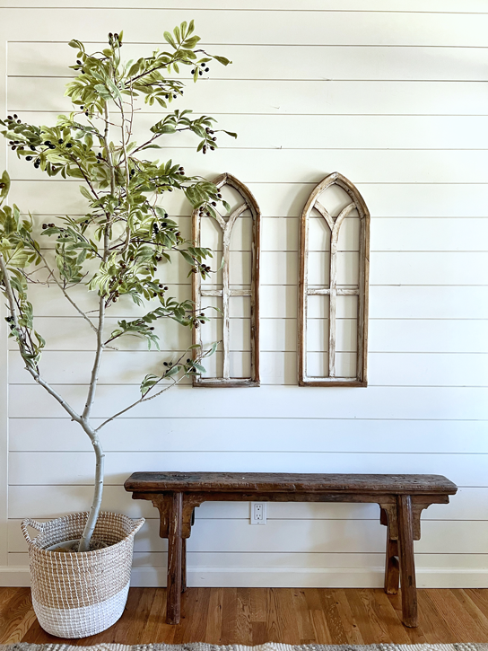 A realistic DIY faux tree is placed next to a rustic wood bench and arched cathedral windows.
