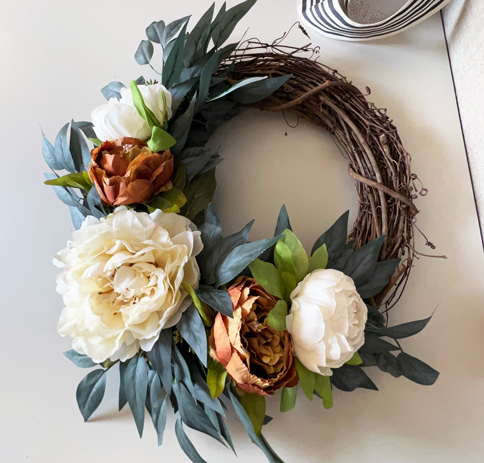 Easy DIY Fall Wreath. Orange and cream peony wreaths hanging with black and white striped ribbon. The wreaths are made of cream, white, and soft orange peonies arranged in a bed of soft dark green eucalyptus. 