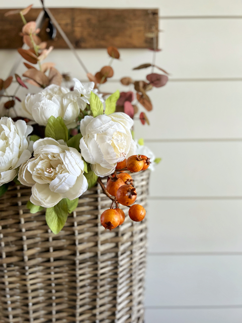 Simple DIY Fall Floral Arrangement made of white peony flowers, orange autumn berry sprigs, and burgundy fall eucalyptus stems hanging in a market basket.
