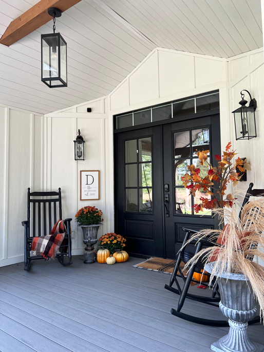 An easy DIY fall tree is placed in a corner of a porch next to a black rocking chair. Black double farmhouse doors, pumpkins, and lanterns surround.