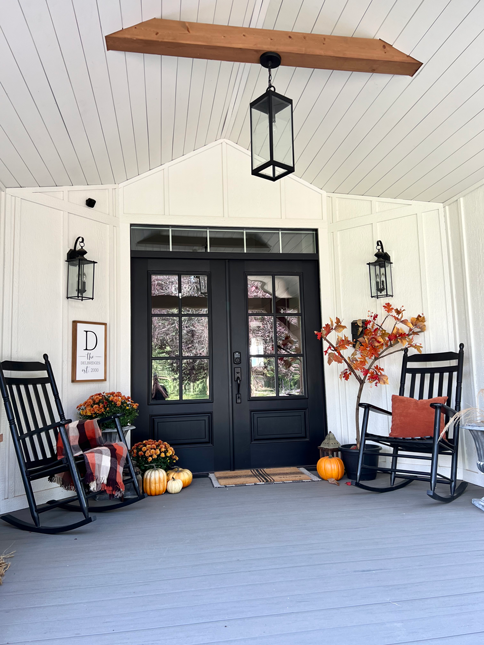An easy DIY fall tree is placed in a corner of a porch next to a black rocking chair. Black double farmhouse doors, pumpkins, and lanterns surround. 