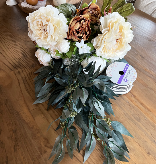 Floral bouquets in soft coffee orange, cream and white with dark green seeded eucalyptus stems and white and black ribbon on a wood table.