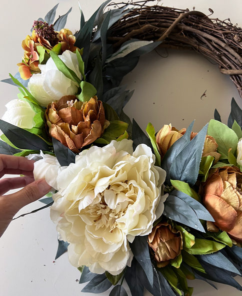 Easy DIY Fall Wreath. Orange and cream peony wreaths hanging with black and white striped ribbon. The wreaths are made of cream, white, and soft orange peonies arranged in a bed of soft dark green eucalyptus. 