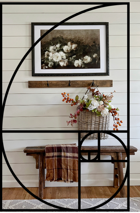 DIY Design and The Golden Ratio golden spiral overlay on a wall with vintage floral art, and wood coat rack with a basket hanging full of orange berries and white roses. A primitive wood bench sits beneath. 