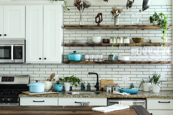 A neutral white kitchen with wood open shelving and white subway tile showcases color use in the golden ratio. Most of the scene is in neutrals and whites, 30% of the scene shows wood tones as contrast. Ten percent of the scene shows a pop of blue color in the cookware. 