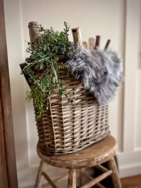 Shiplap and board and batten walls sit as a backdrop to a chippy painted antique stool with a basket of fuax fur, pine, and wood sticks. 