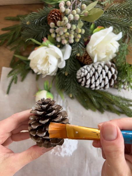 Paint brush painting on adhesive to a pinecone for Easy DIY Winter Frosted Pinecones
