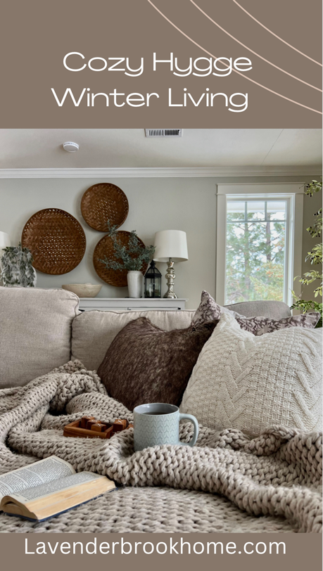 Cozy Hygge-Inspired Winter Living -Cozy couch scene with a beige chunky woven blanket, knit and faux fur pillows. A cup of tea, a book, and a tic tac toe game rest upon the cozy vignette
