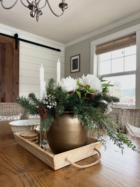 Cozy Hygge-Inspired Winter Living - A bouiquet of pine and white peonies sits on a dining room table with a farmhouse barn door in the background. 
