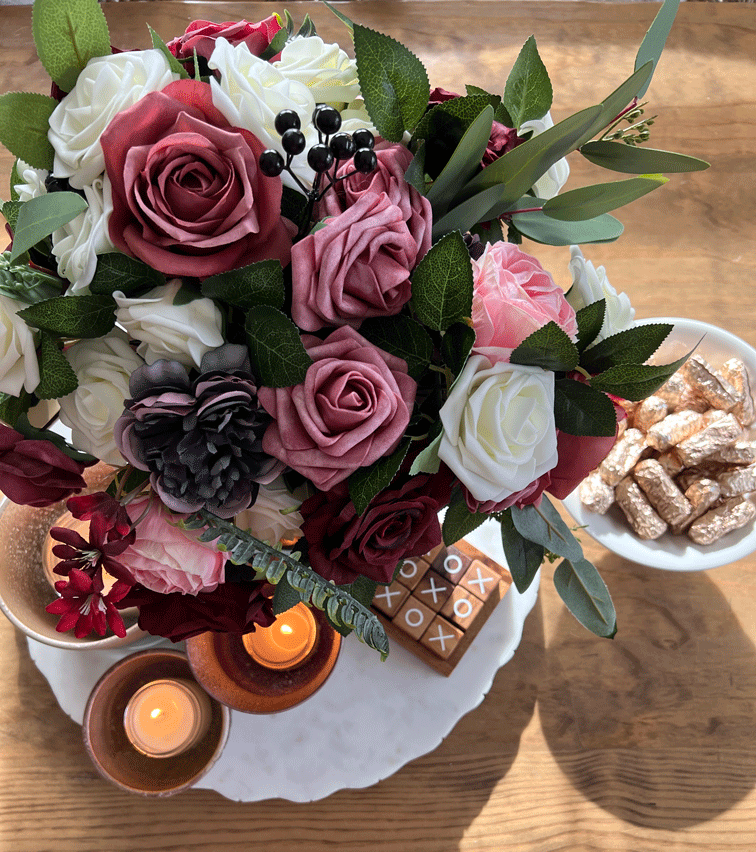 DIY Mercury Glass Candle Holders: Overview of a pink, white, and burgundy rose bouquet with a wood tic tac toe board and gold foiled candies. 
