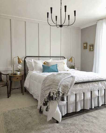 Farmhouse style bedroom with vintage art, gold lamps on wooden round nightstands, and board & batten walls.